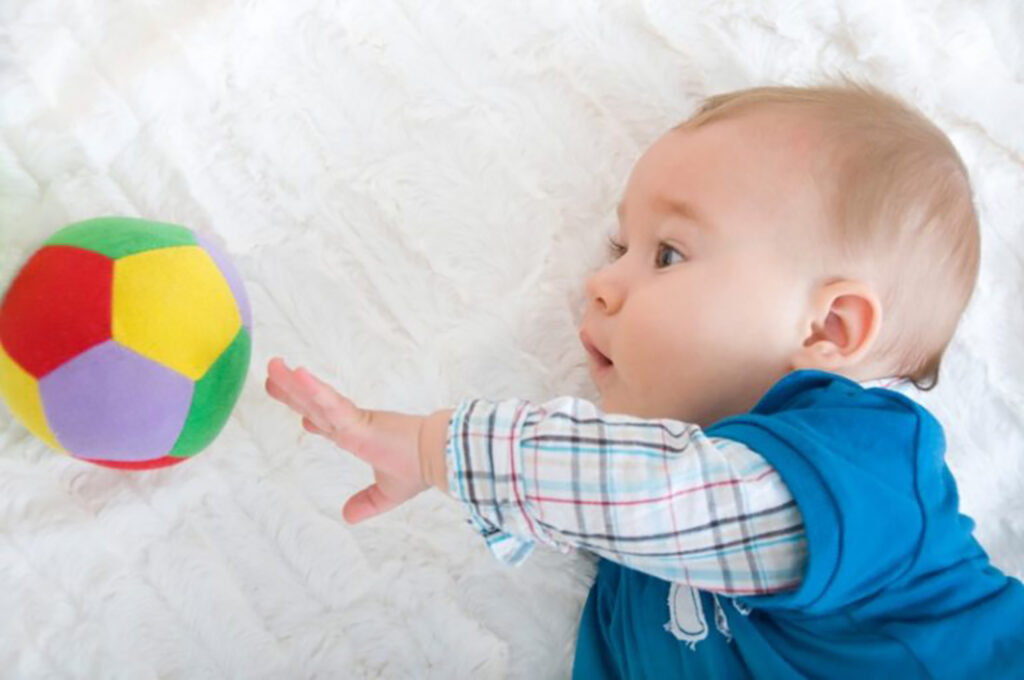 Bebé a brincar com bola na cama 